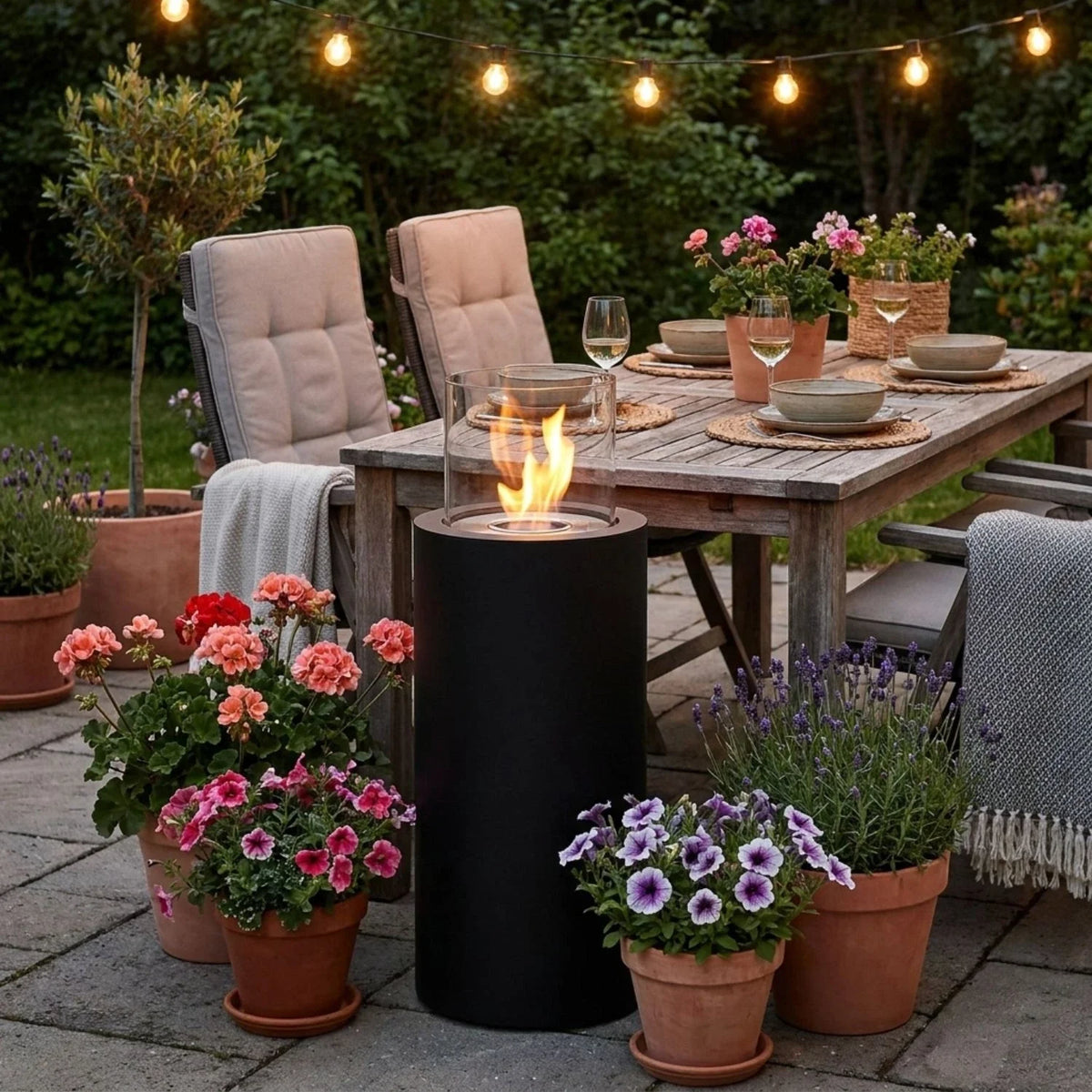 ScandiFlames Dualis Black lit bioethanol fireplace beside a garden dining table surrounded by flowering plants